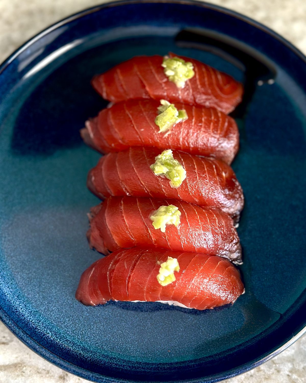 A row of hand-pressed nigiri plated on a blue ceramic dish